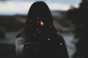 A person holds a sparkler at twilight, creating a magical and mysterious silhouette effect.